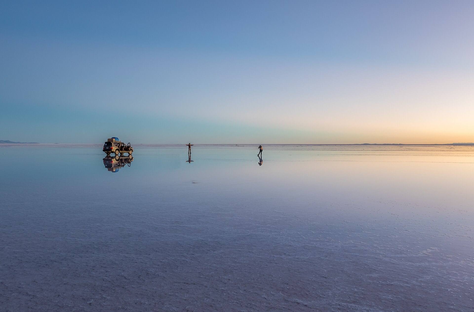 Viajeros y un todoterreno reflejados en el Salar de Uyuni al amanecer